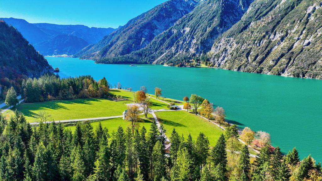 Der Achensee im goldenen Herbstlicht – Blick auf das Achenseehof-Areal, gegenüber die Gaisalm, während ein Schiff den See kreuzt.